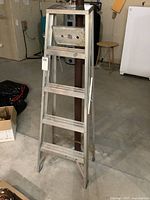 Front view of the 5 foot aluminum step ladder showing five steps and top platform, placed standing open in basement area.