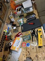 Overview of various tools and hardware items on wooden workbench for sale, including measuring tapes, tape dispenser, scissors, laser level, hot glue gun, and batteries.