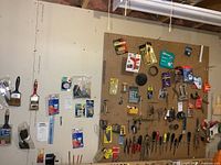 Wide view of wall with pegboard filled with assorted tools, paint brushes, tapes, pliers, screwdrivers, drill bits and packaged items