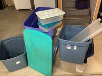 Collection of plastic storage totes of various sizes and colors stacked in basement area. Some lids included.
