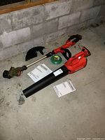 Photo showing both Craftsman cordless leaf blower and string trimmer placed on concrete floor, along with replacement string spool and manuals.