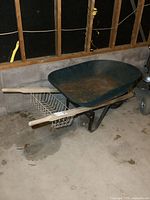 Side view of the metal wheelbarrow showing the green tray, wood handles, and wire basket underneath.