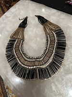 Full view of the Cleopatra collar necklace showing the layered beaded design in black, white, and gold.
