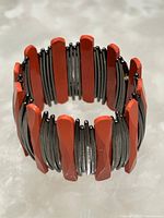 Photo of a cuff bracelet with alternating reddish-orange solid segments and black multi-strand wire sections arranged in a circular form on a white background.