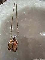 Full image of the gold toned necklace with square Art Deco lucite pendant on a reflective white surface.