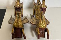 Front view of two gold gilt wooden foo lions with detailed wings and facial features.
