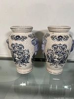 Front view of the pair of crackle glazed ceramic vases showing blue floral and ornamental designs with sculpted side handles.