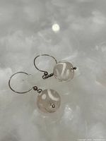 Photo showing a pair of earrings with translucent round glass beads and white swirls on metal hooks, placed on a reflective surface