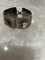 Silver toned bracelet showing clasp and stone accented sunburst design on three linked rectangular segments.