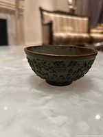 Side view of the cast bronze ritual bowl showing raised floral designs and patina on the exterior.