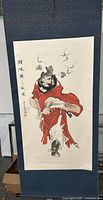 Full image of the Chinese painted scroll showing the figure in red robes on blue fabric backing.