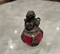 Front angle of paperweight showing the metal lion sitting atop the pink marble sphere with visible metal leaf and floral decoration.