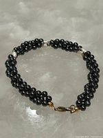Full view of a dark hematite and pearl beaded bracelet laid flat showing the entire strand and clasp.