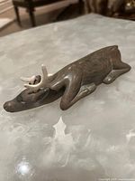 Right side angle view of the small carved stone reindeer on a light reflective surface.