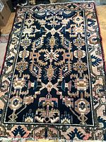 Full view of the rectangular wool rug with dark navy blue background and intricate geometric and floral motifs