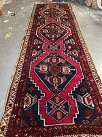 Full-length view of runner laid on concrete floor showing alternating red and navy geometric medallions with ivory border.
