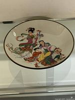 Photo of the full decorative plate showing painted figures in traditional Chinese clothing with vibrant colors and gold rim