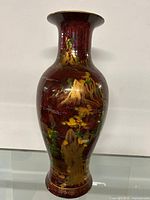 Full front view of tall ceramic vase with landscape painting on deep red background.