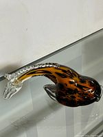 Side view of the Murano style hand blown glass giraffe figurine, showing the elongated clear glass neck with raised clear glass dots and the brown/amber/black swirled body.