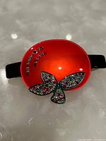 View of the front of the red enamel hairclip with rhinestone decorations in the shape of a leaf or butterfly.