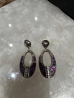 Photo shows pair of silver-tone drop earrings with purple marbled inlay and rhinestone decoration on a reflective surface.