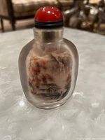 Front view of the Chinese snuff bottle showing reverse painted village scene with house, trees, and a figure near a house with autumn foliage colors.