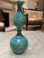 Front angle of the turquoise swirled and floral designed vase on a marble surface.