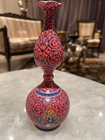 Front view of the hand painted Persian enamel vase showing its rounded body, narrow neck, and flared scalloped rim decorated in red and blue with floral and geometric designs.