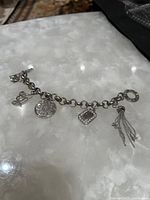 Full view of the silver toned charm bracelet laid out on a white marbled surface, showing all charms.