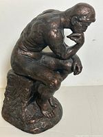 Side angle showing muscular detail and the seated pose of the statue on its textured base.