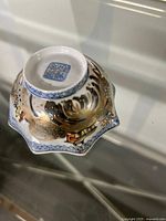 Photo showing the underside of the scalloped porcelain bowl, highlighting the Chinese mark and detailed hand-painted scene on the exterior.