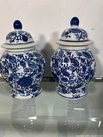 Pair of blue and white Chinese ginger jars with lids, showing floral and vine designs in cobalt blue on white porcelain.