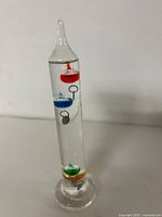 Full view of glass Galileo thermometer showing coloured bulbs