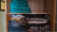Cupboard shelf with stacks of teal, grey, mauve and animal print towels