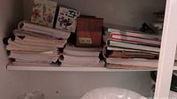 Shelf with stacked loose recipe pages, binders, two recipe card boxes (floral metal and wood)
