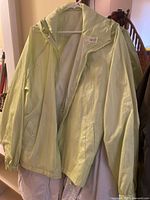 Front view of light green jacket on hanger showing full shape, zipper, pockets, sleeves