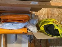 Shelf with folded orange tarp, folded white tarp, additional bagged tarps