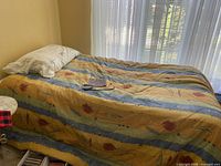 Single bed fully made with comforter and pillow next to window