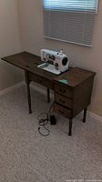 Sewing machine atop wooden cabinet table, drawers closed