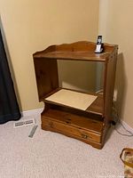 Front view of wood cabinet showing open compartment, shelf, drawer and phone for scale
