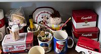Shelf with assorted Campbell's tins, mugs, plush dolls and plate