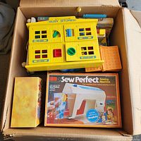 Box containing yellow Busy Stores playset, boxed Sew Perfect sewing machine, orange plastic case