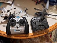 Both RC helicopters and their controllers on table