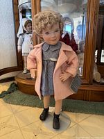 Front view of standing doll with pink coat and blue gingham dress