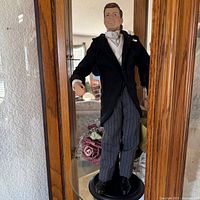 Front view of John F. Kennedy doll in tuxedo on stand inside display cabinet