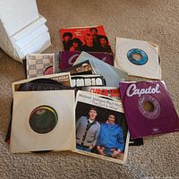 Assorted 45 rpm records in various company sleeves and picture sleeves on carpet