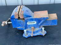 Mastercraft 5-inch bench vise side and front view showing metal jaws, rotating base with bolts, and screw handle.