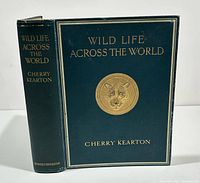 Front cover of dark green full cloth hardcover book titled Wild Life Across the World by Cherry Kearton with gilt embossed lion head motif on front board and gilt text on spine.