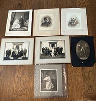 Overview of all 7 antique photographs together on wooden floor showing various portraits and group images in different mounting styles.