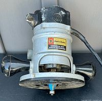 Front and top view of metal-bodied Black & Decker commercial router showing label, dual handles, power cord, and base plate with installed blue router bit.